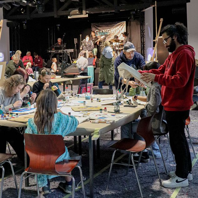 Menschen unterschiedlicher Herkunft und Alters machen gemeinsam Kunst im Hintergrund spielt die inklusive Band Gangway